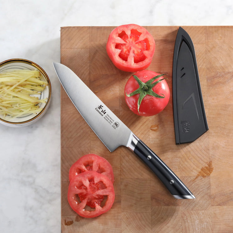 5.5-inch utility knife with black handle and protective sheath on wooden cutting board with whole and sliced tomatoes.