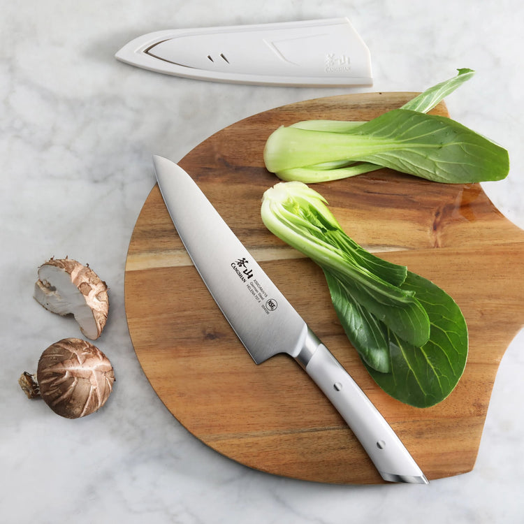 5.5-inch utility knife with white handle on wooden cutting board with bok choy and mushrooms, blade cover nearby.