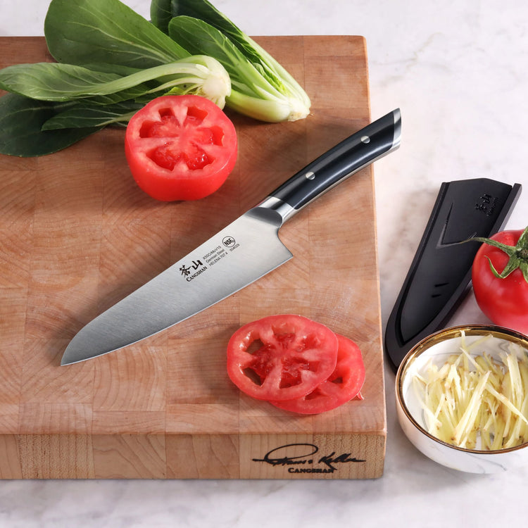 5.5-inch utility knife with black handle on wooden cutting board next to sliced tomatoes and leafy greens.