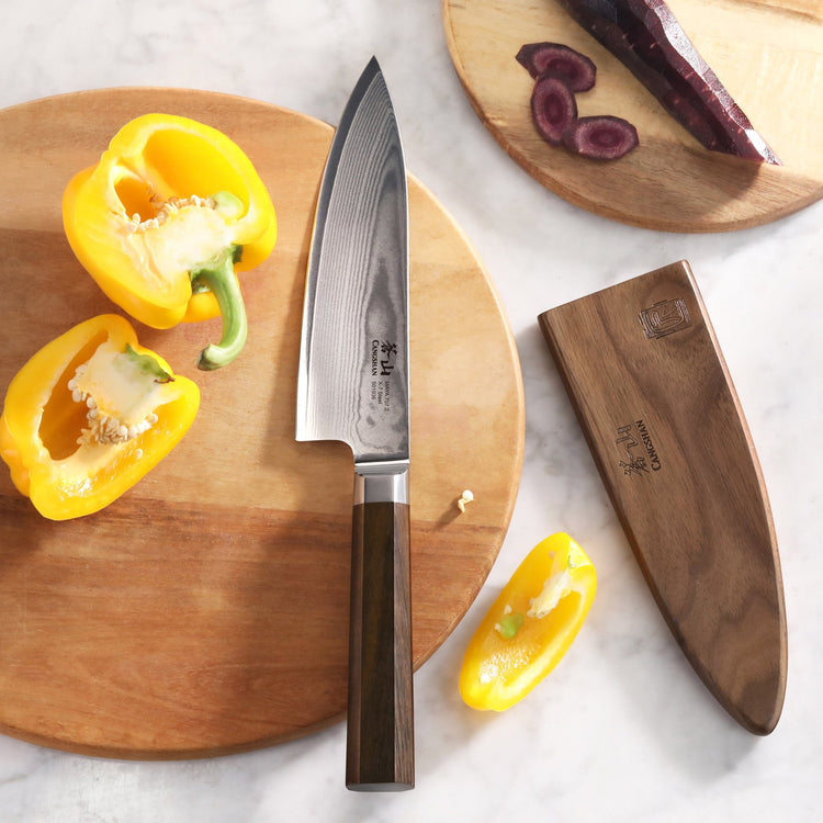 MAYA Series 6-Inch Chef’s Knife X-7 Damascus Steel with a dark wooden handle, wooden sheath, and yellow bell peppers.