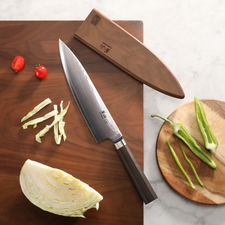 MAYA Series 8-Inch Chef’s Knife X-7 Damascus Steel with a wooden sheath on a cutting board next to sliced vegetables.