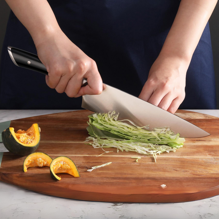 Hands slicing cabbage on a wooden cutting board with cut pumpkin pieces nearby.