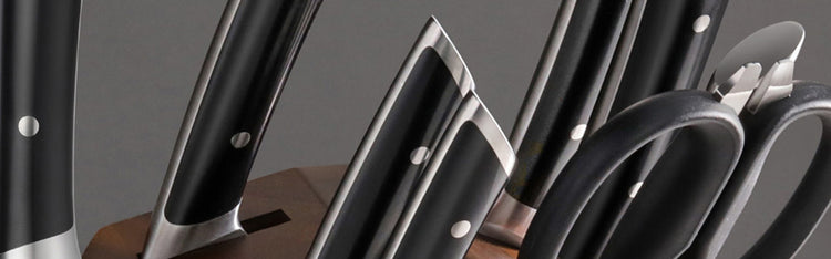 Set of kitchen knives and scissors with black handles in a wooden knife block against a dark background.