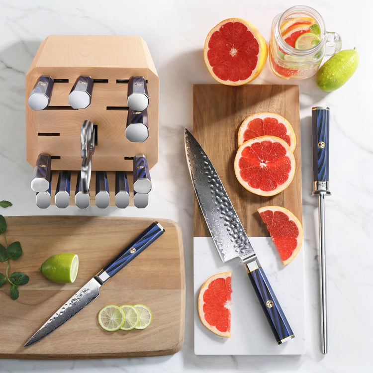 Knife block with empty slots, two knives with blue handles, sliced grapefruit and lime on wooden and marble boards.