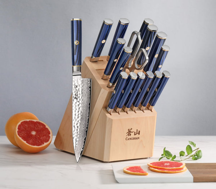 Knife block set with blue-handled knives, one knife displayed outside, next to sliced grapefruit and herbs.