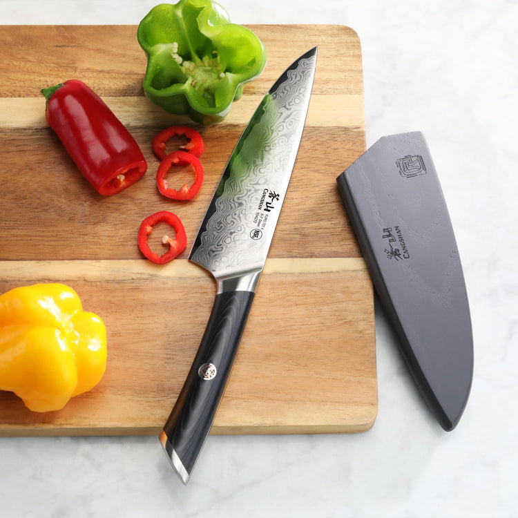 6-inch chef's knife with patterned blade and black handle on wooden cutting board with sliced red pepper and whole green and
