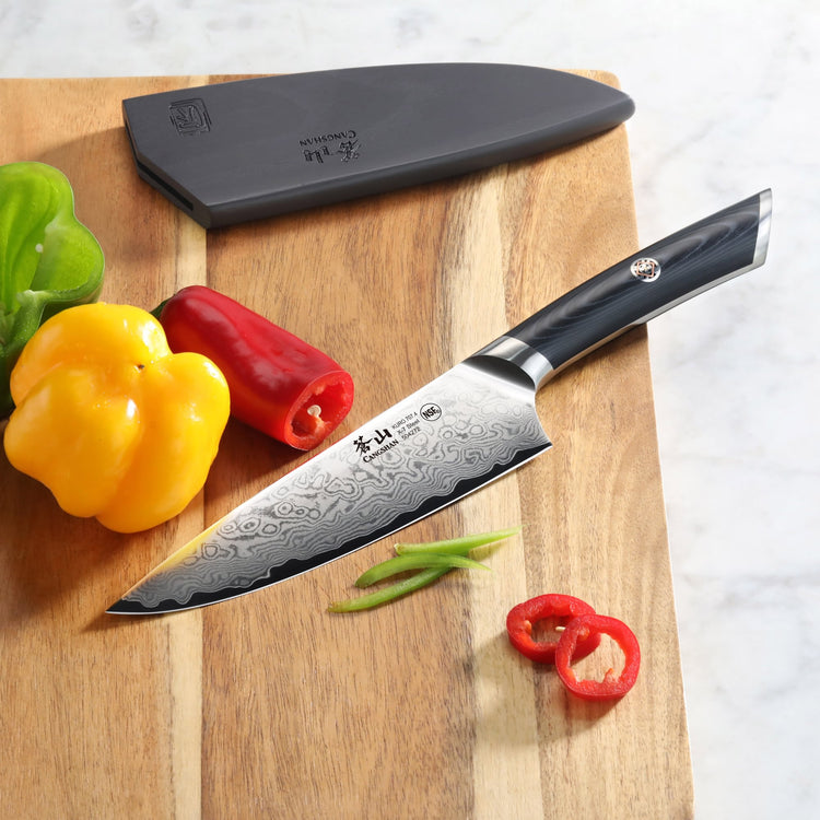 6-inch Damascus steel chef's knife with black handle on wooden cutting board next to sliced and whole bell peppers.