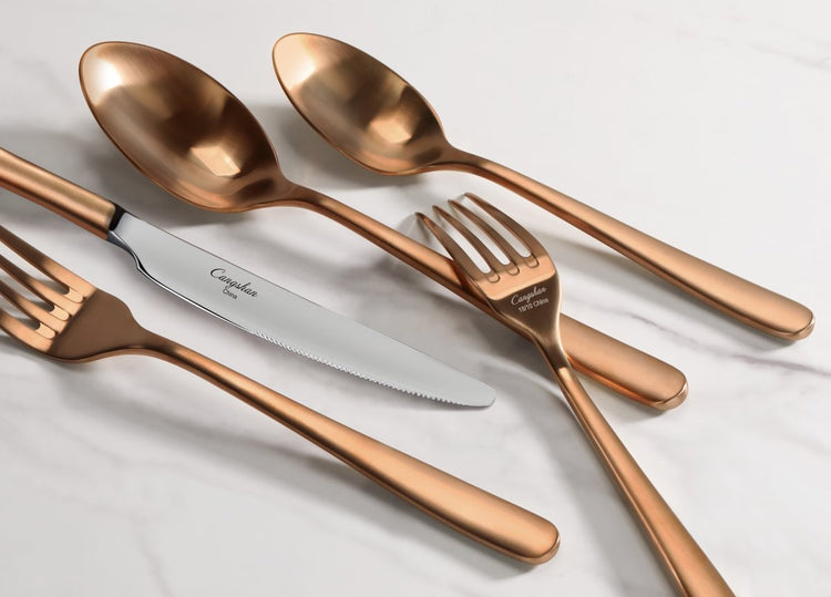 Copper-colored RAIN II Series forged flatware set with spoons, forks, and a knife on white marble.