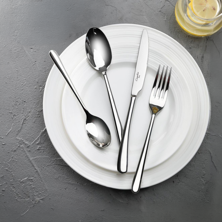 Four-piece polished stainless steel flatware set resting on white ceramic plates.