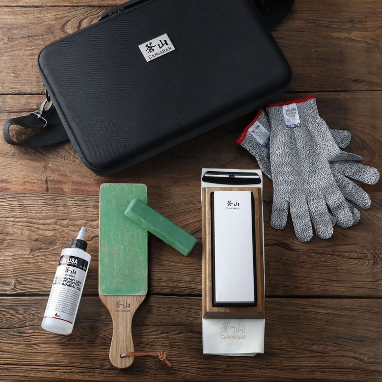 Black carrying case, sharpening stone with wooden base, honing paddle with green stone, sharpening oil bottle, and cut-resist