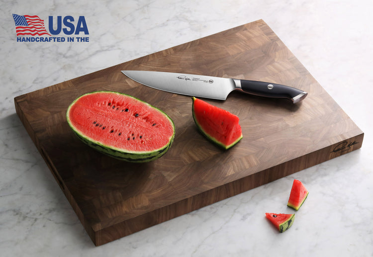 Walnut end-grain cutting board with a chef's knife and sliced watermelon on a marble surface.