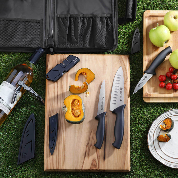 Seven-piece travel knife set with black handles, including a sharpener and blade covers, displayed on wooden boards with cut
