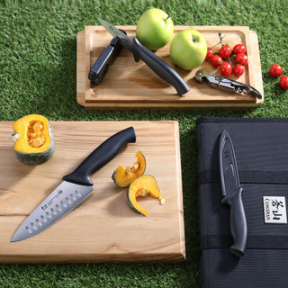 
                    
                      Seven-piece travel knife set with black bag, including chef's knife, paring knife, and corkscrew on wooden boards with fruit.
                    
                  
