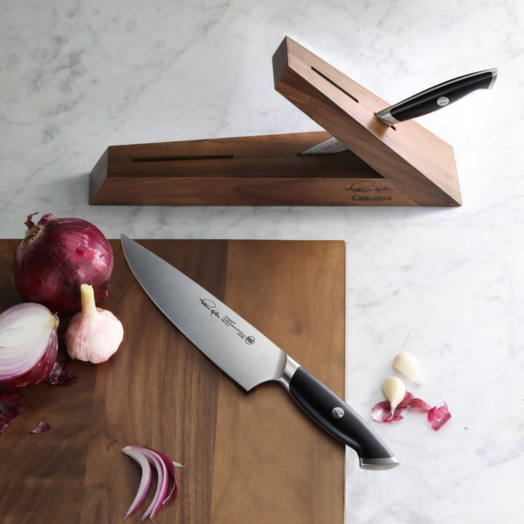 Three-piece knife block set with two knives inserted and one knife on a wooden cutting board next to onions and garlic.