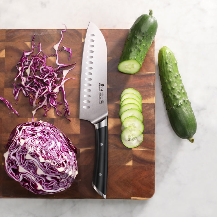 Santoku knife on wooden cutting board with sliced cucumber and shredded purple cabbage.