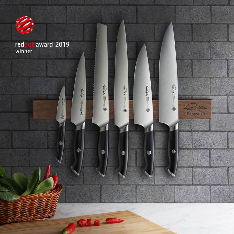 Seven black-handled knives with stainless steel blades mounted on a wooden magnetic strip against a gray tiled wall.