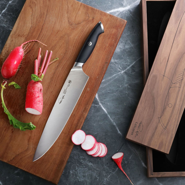 10-inch chef knife with black handle on wooden cutting board next to sliced radishes and wooden storage box.
