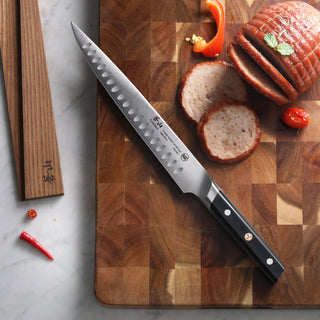 
                    
                      Japanese-style chef knife with a black handle on a wooden cutting board next to sliced cooked meat.
                    
                  