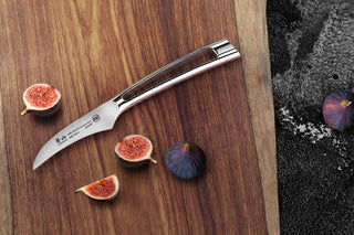 
                    
                      Curved peeling knife with stainless steel handle on wooden board next to whole and sliced figs.
                    
                  