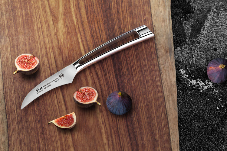 Curved peeling knife with stainless steel handle on wooden board next to whole and sliced figs.