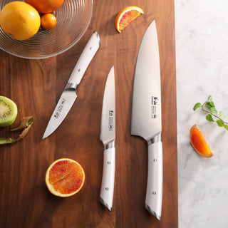 
                    
                      Three stainless steel kitchen knives with white handles arranged on a wooden cutting board next to sliced citrus fruits and a
                    
                  