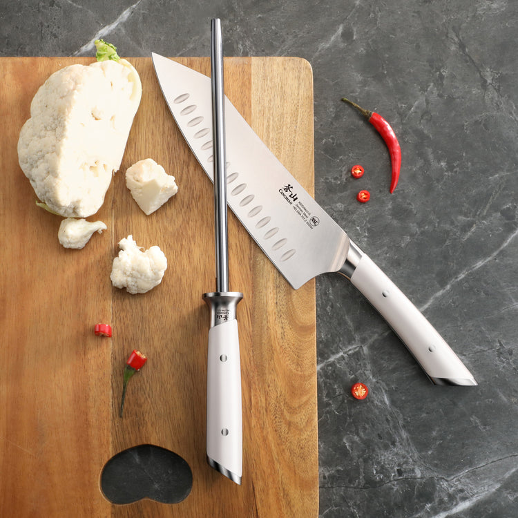 8-inch honing steel with white handle next to a chef's knife on a wooden cutting board with cauliflower and red chili peppers