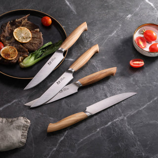
                    
                      Four steak knives with wooden handles arranged on a dark surface next to a plate with cooked meat, lemon slices, and vegetabl
                    
                  
