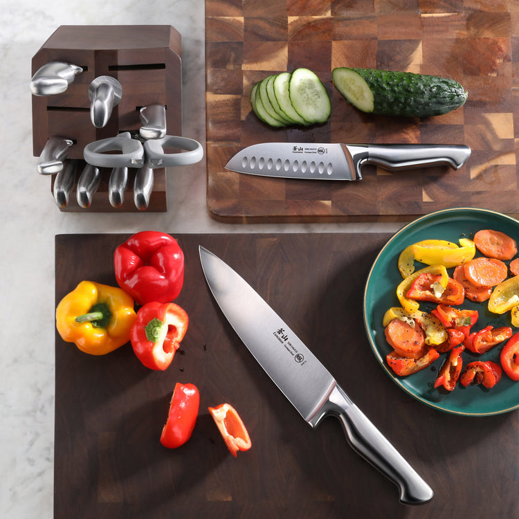 Knife block with knives, a sliced cucumber on a cutting board, and a chef knife with sliced bell peppers on a dark board.
