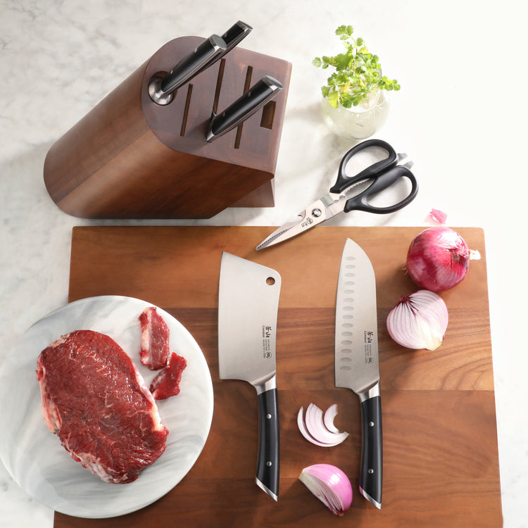 Knife block set with two knives and scissors on a wooden cutting board, alongside raw meat and sliced red onions.