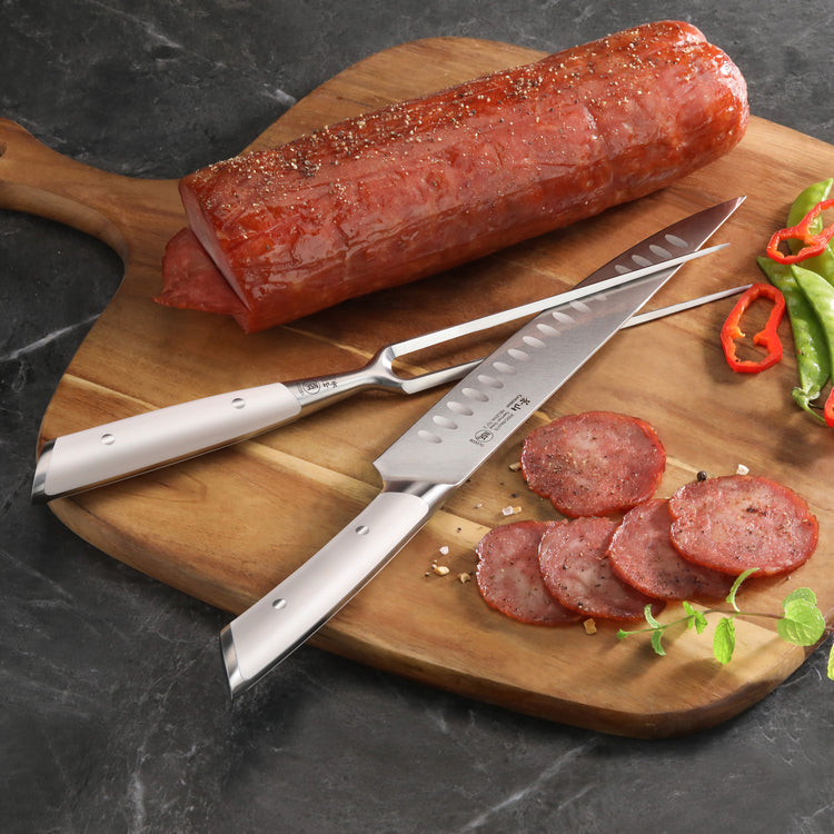 Two-piece carving set with a knife and fork slicing seasoned cooked meat on a wooden cutting board.