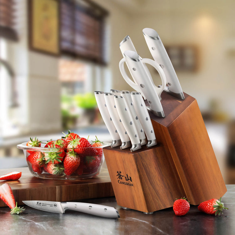 Wooden knife block holding white-handled knives and kitchen scissors, with a bowl of strawberries nearby.