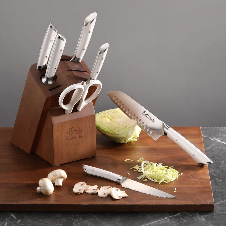 Knife block set with five knives and scissors in acacia wood block, two knives on cutting board with sliced mushrooms and cab