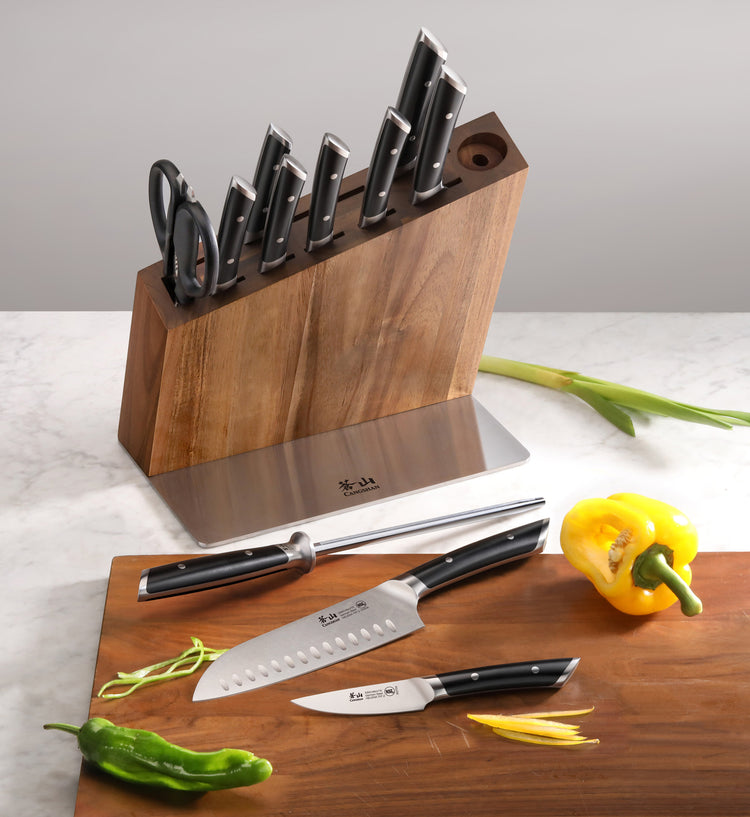 12-piece knife set with black handles in acacia wood block, including scissors and three knives on a wooden board with vegeta
