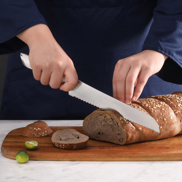 Person slicing a seeded loaf of bread on a wooden cutting board with a serrated bread knife.