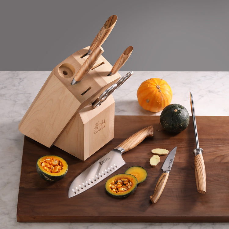 Wooden knife block with four knives inserted, two cut pumpkins, and a sharpening steel on a wooden cutting board.