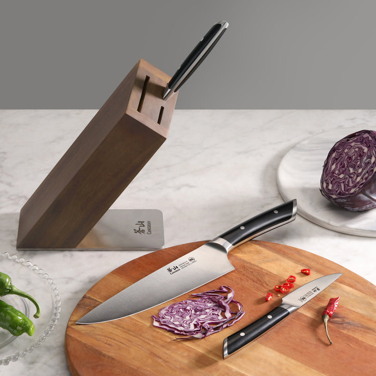 Six-piece knife set with two knives on a wooden cutting board, a wooden block, and sliced red cabbage and chili peppers.