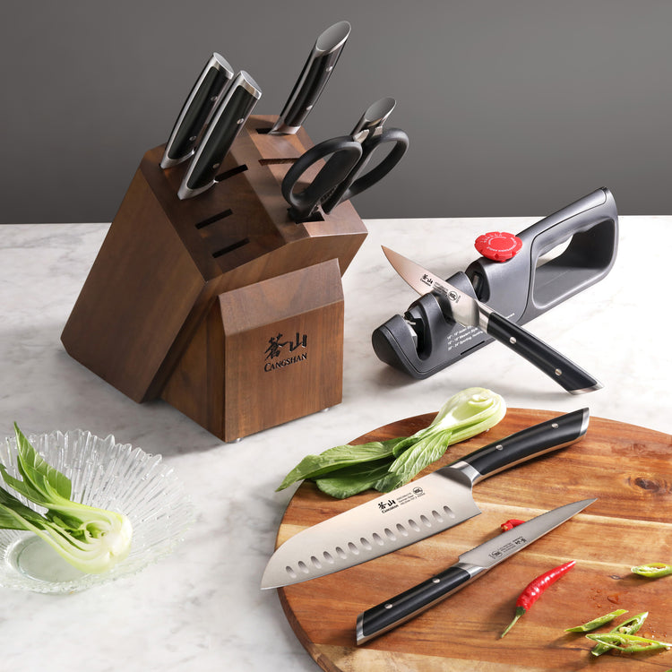 Knife block set with five knives and kitchen scissors in an acacia wood block, knife sharpener, and vegetables on a cutting b