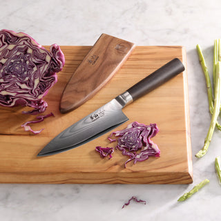 
                    
                      6-inch chef's knife with patterned blade and black handle on wooden cutting board with purple cabbage and sheath nearby.
                    
                  