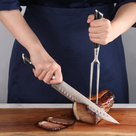 Person carving a cooked meat roast on a wooden cutting board using a carving knife and fork with black handles.
