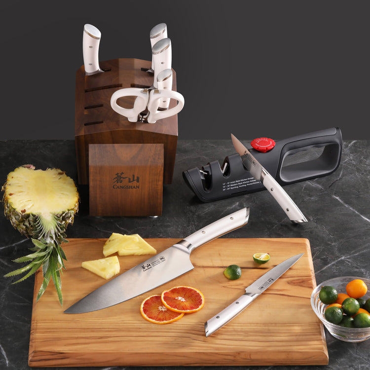Knife block set with five knives and scissors in acacia wood block, two knives on cutting board with sliced citrus and pineap