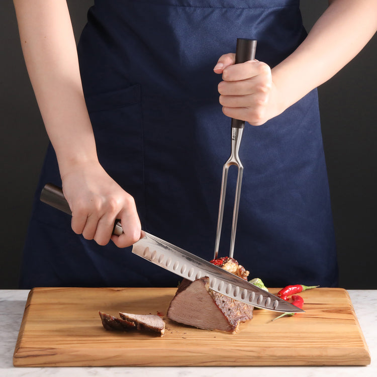 Person carving a cooked roast on a wooden cutting board using a carving fork and knife with dark handles.