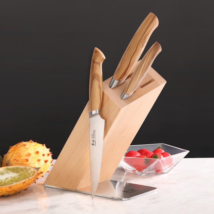 Four-piece knife block set with wooden handles in a maple block on a marble surface, next to fruit and tomatoes.