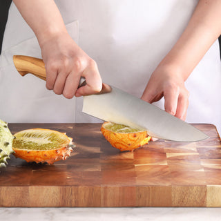 
                    
                      Hand holding a knife with a maple handle, slicing a horned melon on a wooden cutting board.
                    
                  