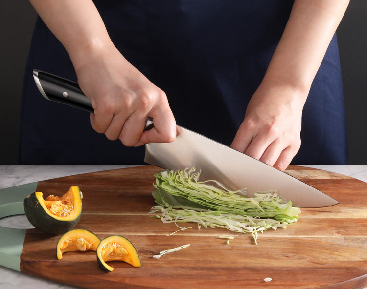 Person slicing cabbage on a wooden cutting board with a forged German steel knife.
