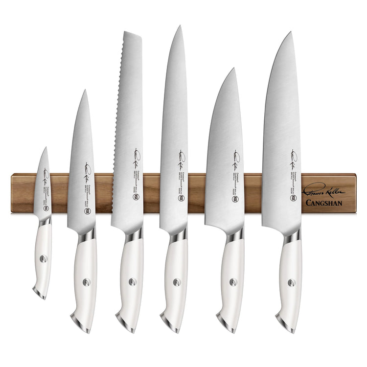 Seven white-handled knives with stainless steel blades displayed on a walnut magnetic knife bar.