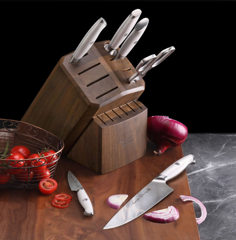 Wooden knife block holding five stainless steel knives with white handles, placed on a wooden surface with sliced red onion a